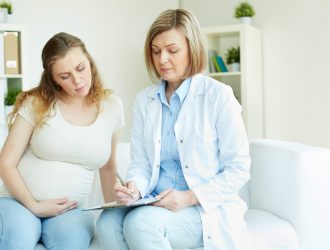 Young pregnant woman listening to prescription of doctor after regular examination at hospital